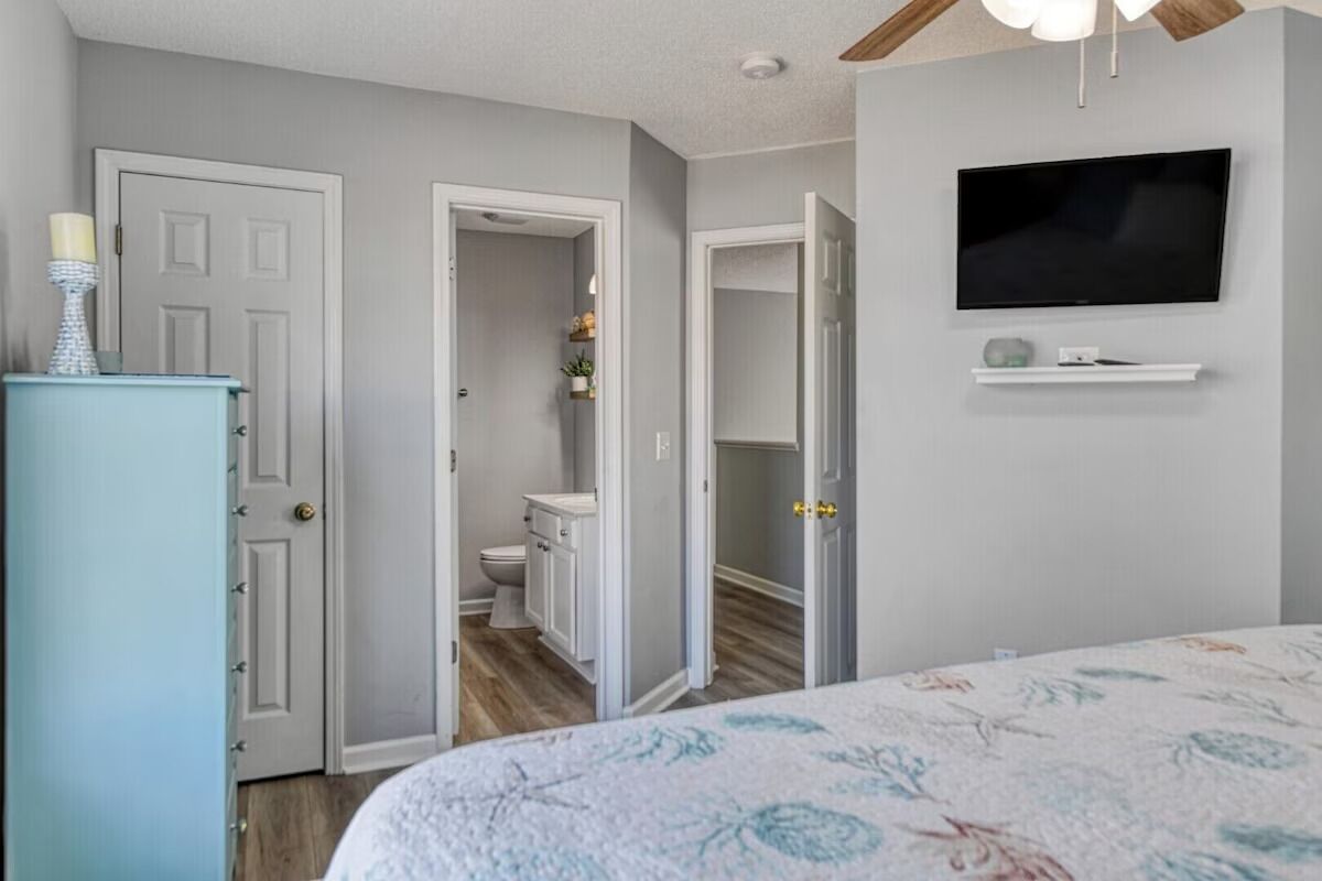 A bedroom with a bed, a television mounted on the wall, and a door leading to a bathroom.