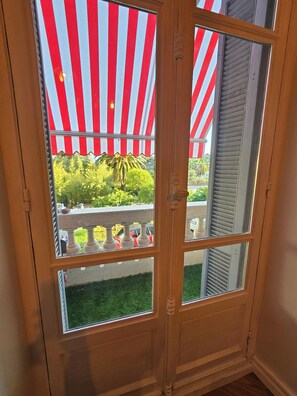 A wooden door with a view of a balcony and a red and white striped awning. - Stay in a Belle Epoque Palace on the French Riviera (Menton)
