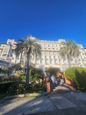 A grand hotel with a central staircase leading to the entrance, surrounded by lush greenery and palm trees. - Stay in a Belle Epoque Palace on the French Riviera (Menton)