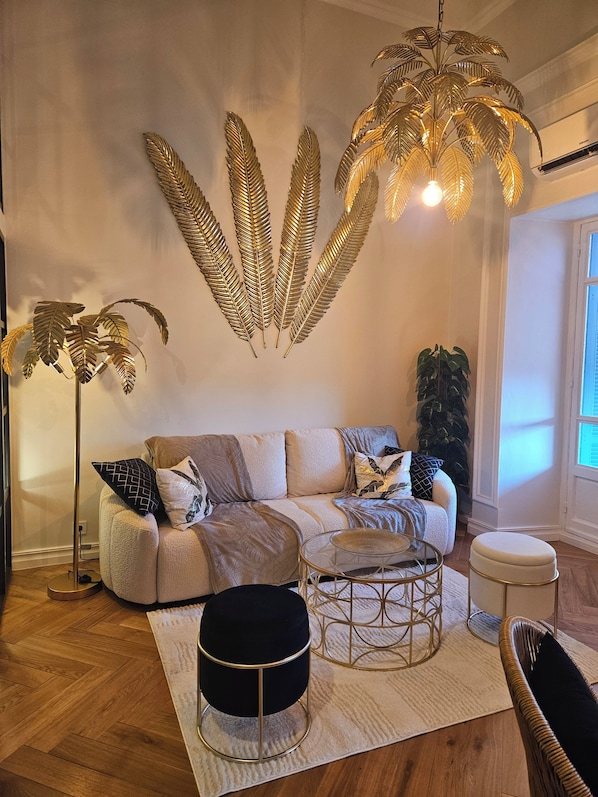 A living room with a sofa, ottoman, floor lamp, and decorative wall art. - Stay in a Belle Epoque Palace on the French Riviera (Menton)