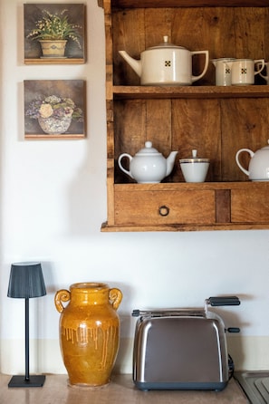 Eine Küche mit einem Holzbodenregal, auf dem weiße Teekannen und Tassen, eine braune Keramikkanne und ein Toaster stehen.