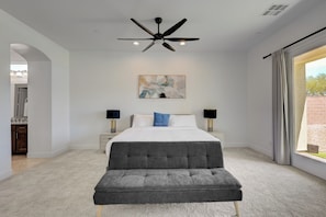 Quarto com cama, luminárias de cabeceira, ventilador de teto, pintura e janela com cortinas.