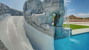 Una piscina con tobogán, cielo azul despejado y un edificio al fondo.