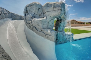 Ein Pool mit Wasserrutsche, wolkenloser, strahlend blauer Himmel und ein Gebäude im Hintergrund.