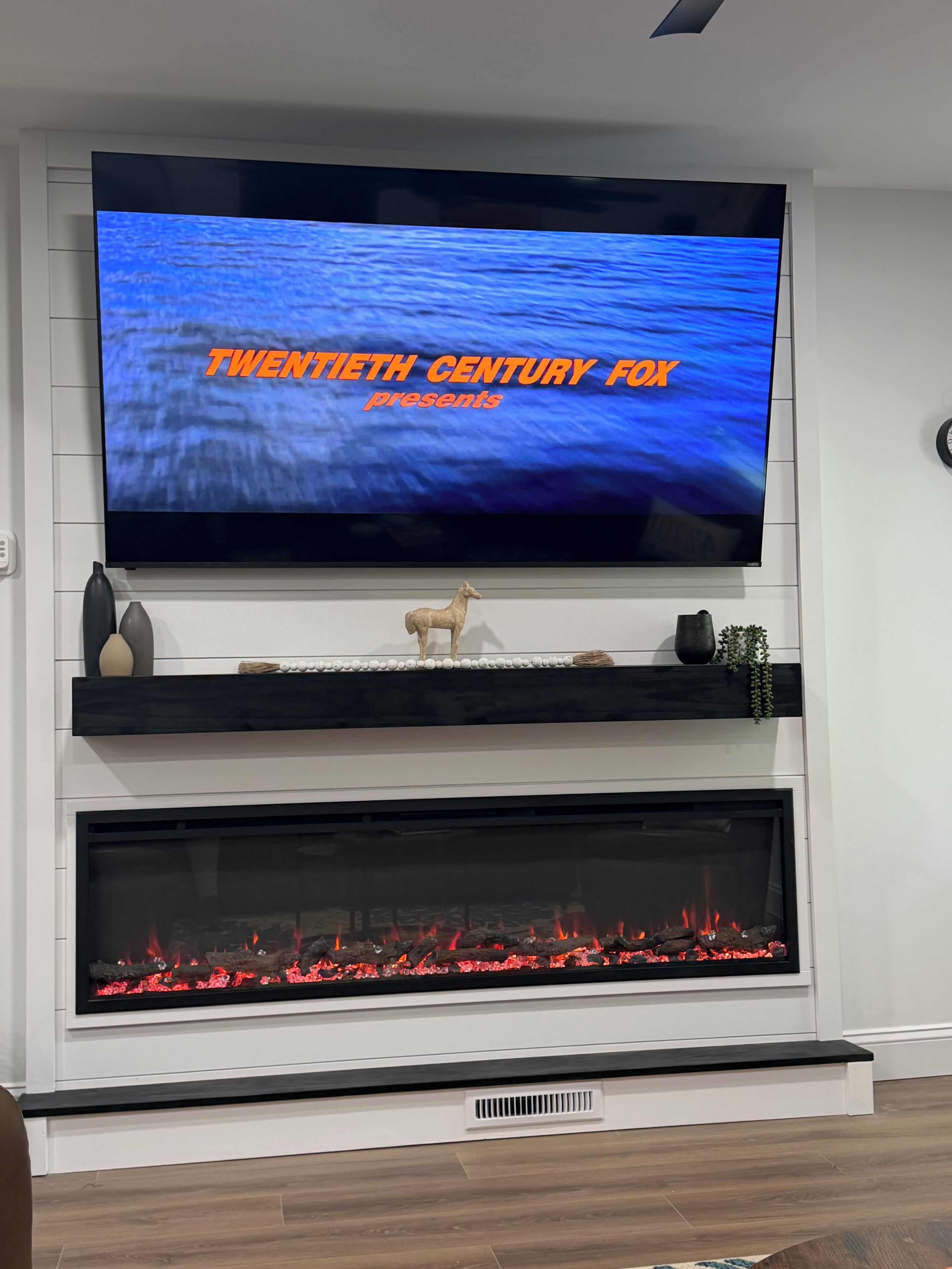 Seinälle asennettu litteänäyttöinen televisio, jonka yläpuolella on takka ja jonka alla on koristeellinen hylly.