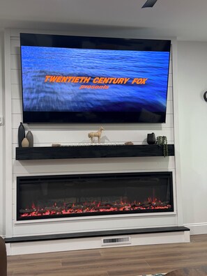 A flat-screen TV mounted above a fireplace with a decorative shelf below.
