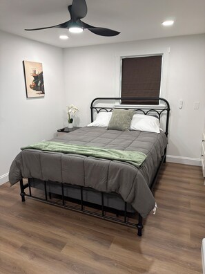 A bedroom with a bed, a ceiling fan, a bedside table with a plant, and a window with a blind. - Encore Retreat, home away from home with extra, including ev charging (Elizabethtown)