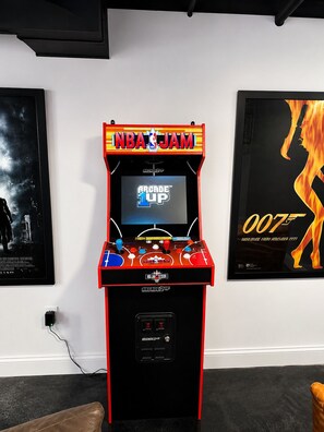 An arcade machine with 'NBA JAM' branding, a '007' poster, and a 'NBA JAM SESSION' sign.