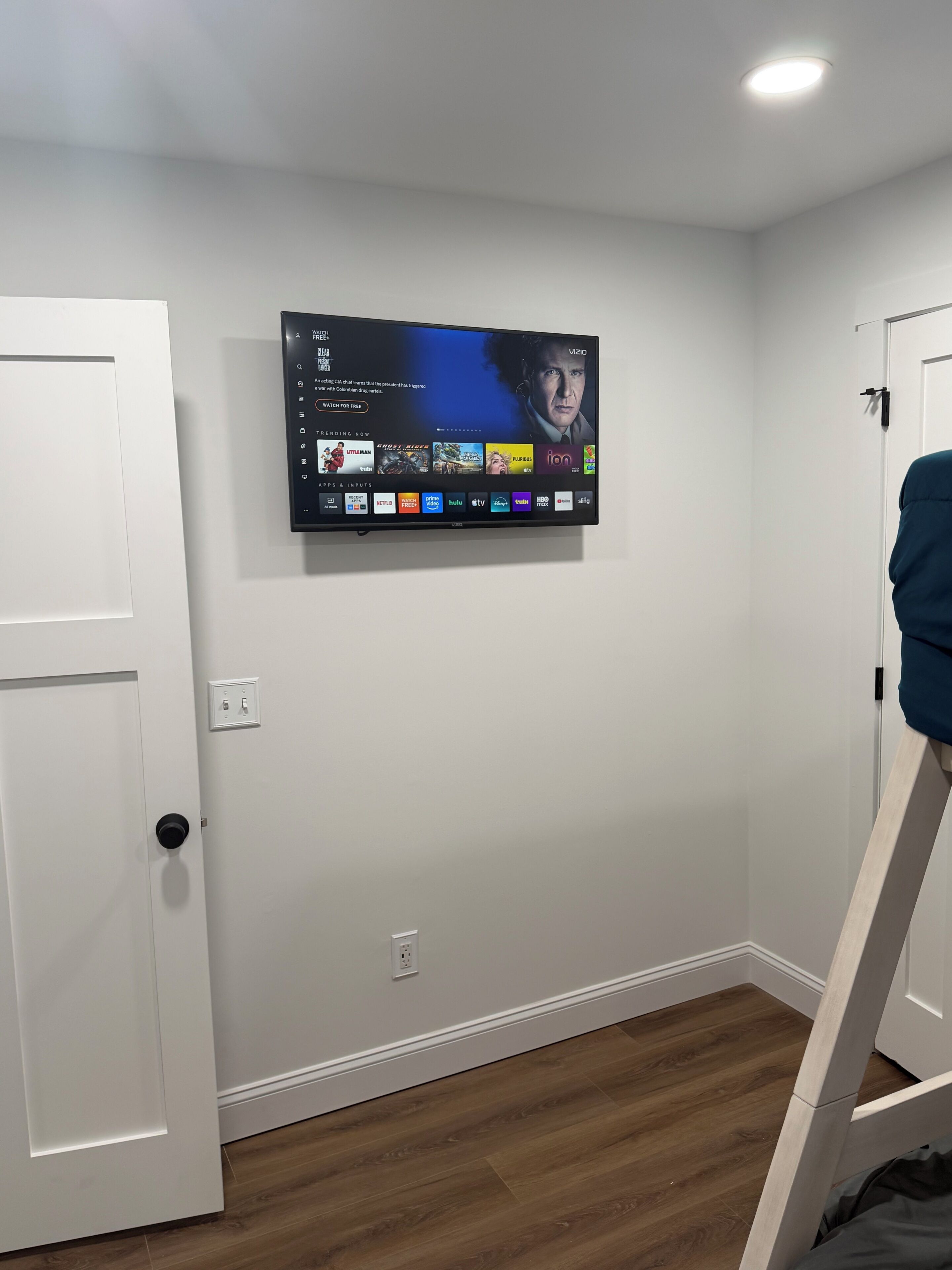 Ein an der Wand befestigter Flachbildfernseher mit Menüoberfläche, eine weiße Tür und ein Holzboden.