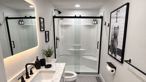 Un baño moderno con ducha envuelta en vidrio, lavamanos de mármol y retrete.