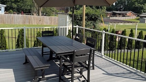 Una terraza con una mesa y bancos, rodeada por una cerca blanca y vista a una zona residencial.