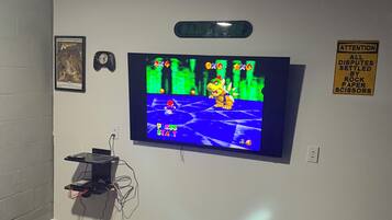 A gaming room with a television displaying a video game, a clock, and a sign on the wall.