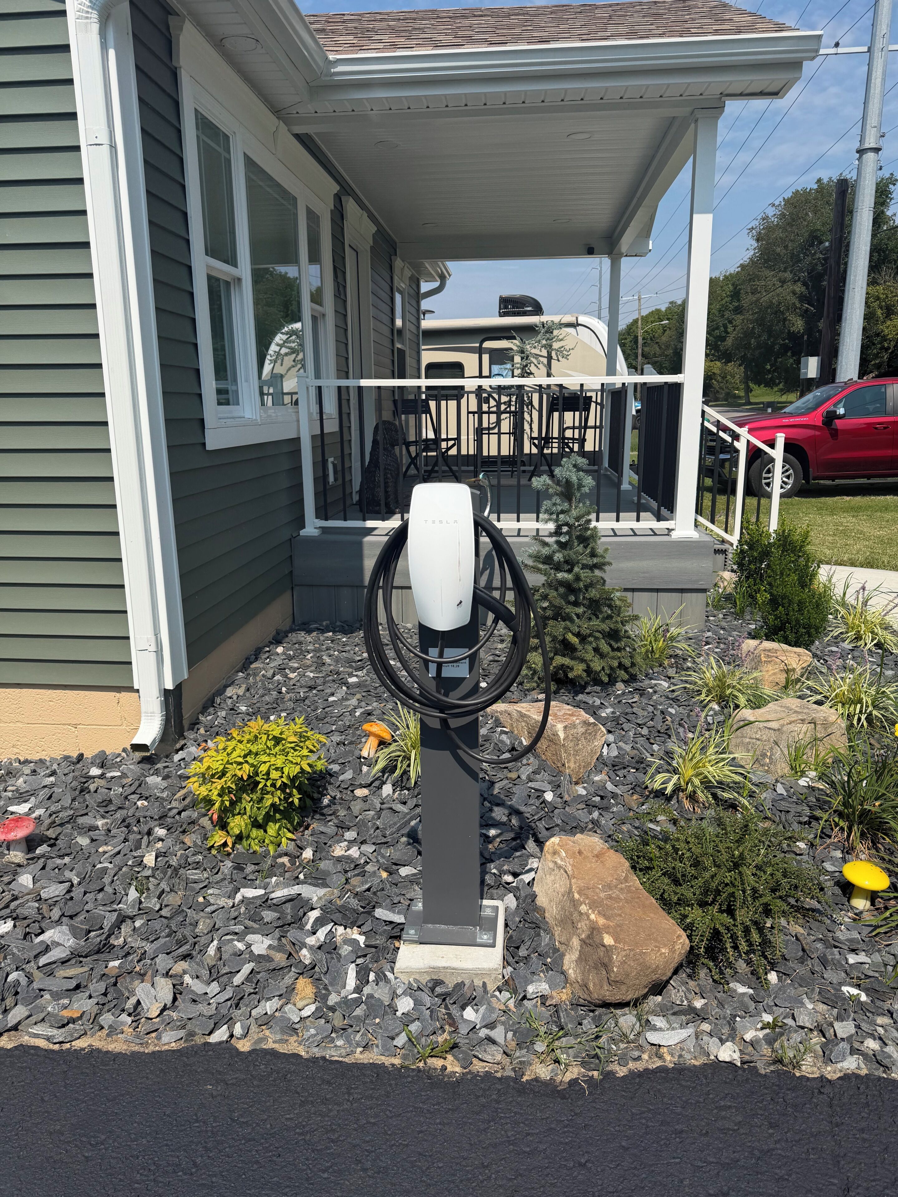 A residential property with a covered porch, a Tesla charging station, and a landscaped garden with rocks and plants.