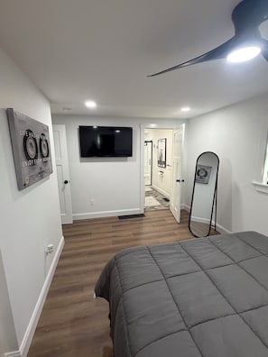 Een slaapkamer met een bed, een plafondventilator, een flatscreen-tv en een spiegel.