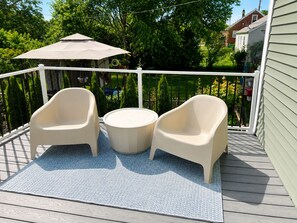 A deck with two chairs and a round table, surrounded by a white railing, with a view of greenery and a house in the background. - Encore Retreat, home away from home with extra, including ev charging (Elizabethtown)