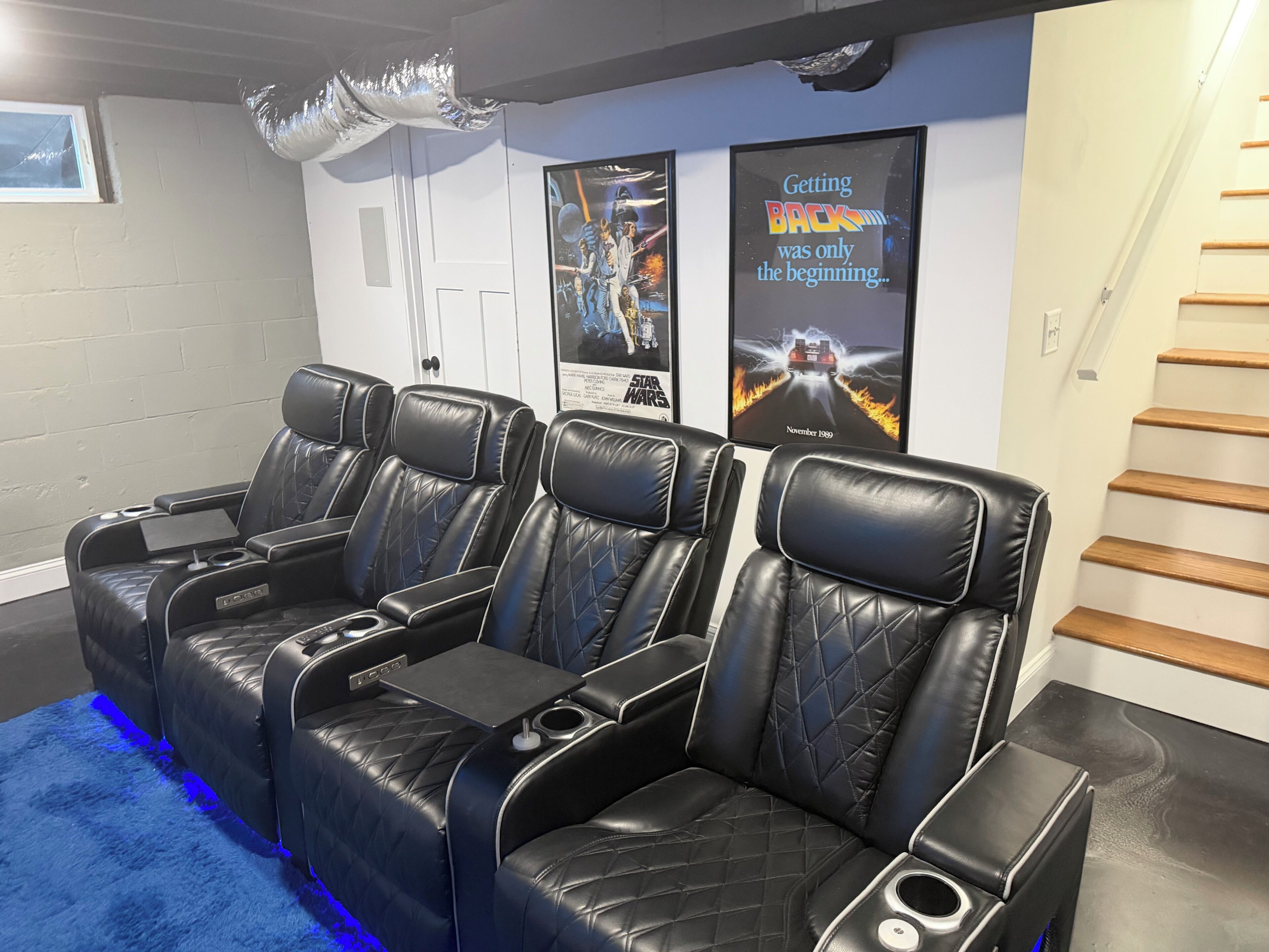 Una sala de cine en casa con cuatro butacas de cuero negro reclinables, una alfombra azul y carteles de Star Wars en la pared.