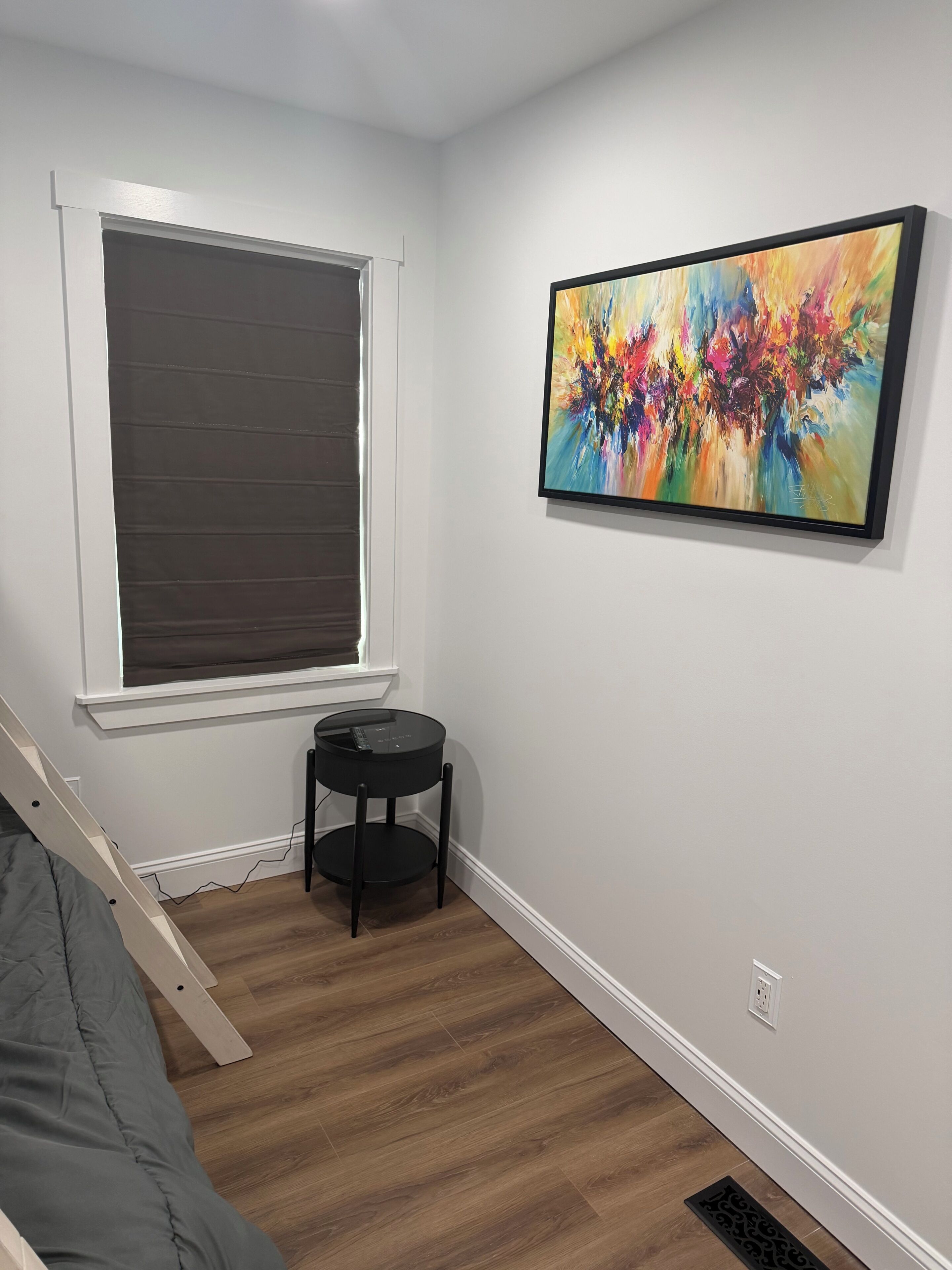 A room with a window, a painting, a small table, and a bed.
