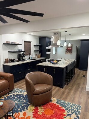 A modern kitchen with dark cabinetry, a central island, and a seating area with a patterned rug. - Encore Retreat, home away from home with extra, including ev charging (Elizabethtown)