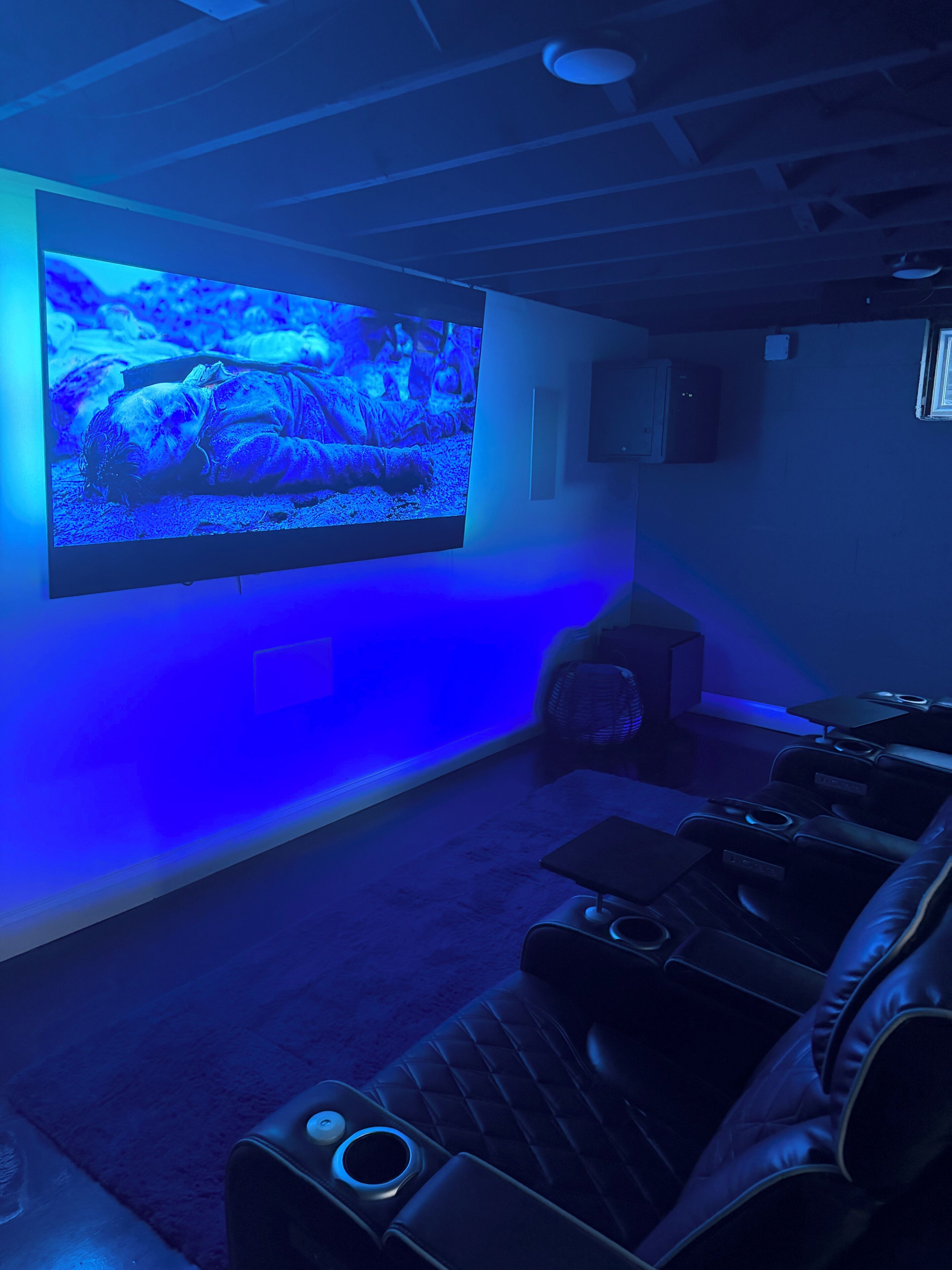 A home theater room with a large flat-screen TV mounted on the wall, leather reclining chairs, and a carpeted floor.