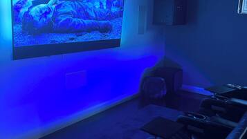 A home theater room with a large flat-screen TV mounted on the wall, leather reclining chairs, and a carpeted floor.