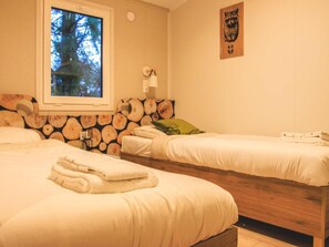 Ein Schlafzimmer mit zwei Betten, einem Fenster mit Blick auf Bäume, einer Wand mit Holzvertäfelung und einem Wandbild.