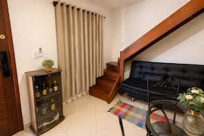 A living room with a black sofa, wooden staircase, and a glass cabinet with bottles.