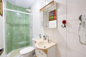 A bathroom with a shower, toilet, sink, and a hairdryer mounted on the wall. - Charming Chalet in the Penedo Mountains (Itatiaia)