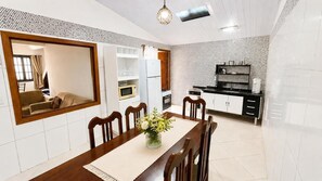 A dining area with a wooden table, chairs, and a vase of flowers. There is a kitchen in the background with a refrigerator, microwave, and stove. - Charming Chalet in the Penedo Mountains (Itatiaia)