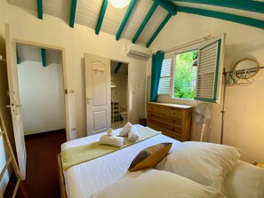 A bedroom with a bed, a dresser, a window with shutters, and an air conditioning unit. - Sea and pool view, fully equipped villa for 8 (Les Trois-Ilets)