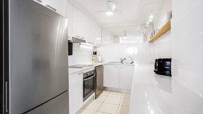 A modern kitchen with stainless steel appliances, white cabinetry, and a black coffee machine. - Porta Pacifique 19 - Beachfront Bilinga - Min. 3 Night Stays - Linen Provided (Bilinga)