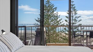 Een slaapkamer met een groot raam dat uitkijkt op een strand en bos.