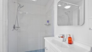 Een moderne badkamer met een glazen douchecabine, een wit wastafelmeubel met één kraan en een spiegel boven de wastafel.