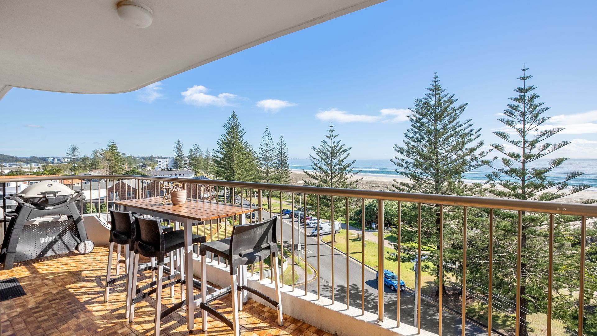 A balcony with a table and chairs, overlooking a beach and ocean.
