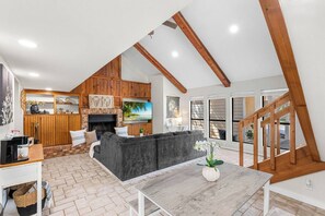 A spacious living area with a fireplace, a large gray sofa, and a wooden staircase. - Charming 2BR Home | Fireplace & Outdoor Lounge (Abilene)