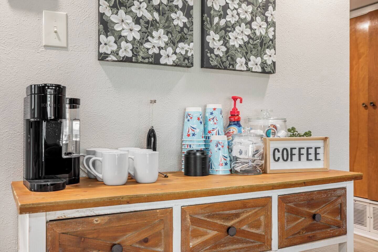 A coffee station with a coffee maker, mugs, and a sign that says 'COFFEE'.