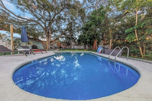 Ein Swimmingpool mit umlaufender Sonnenterrasse, Liegestühlen und einem überdachten Sitzbereich.