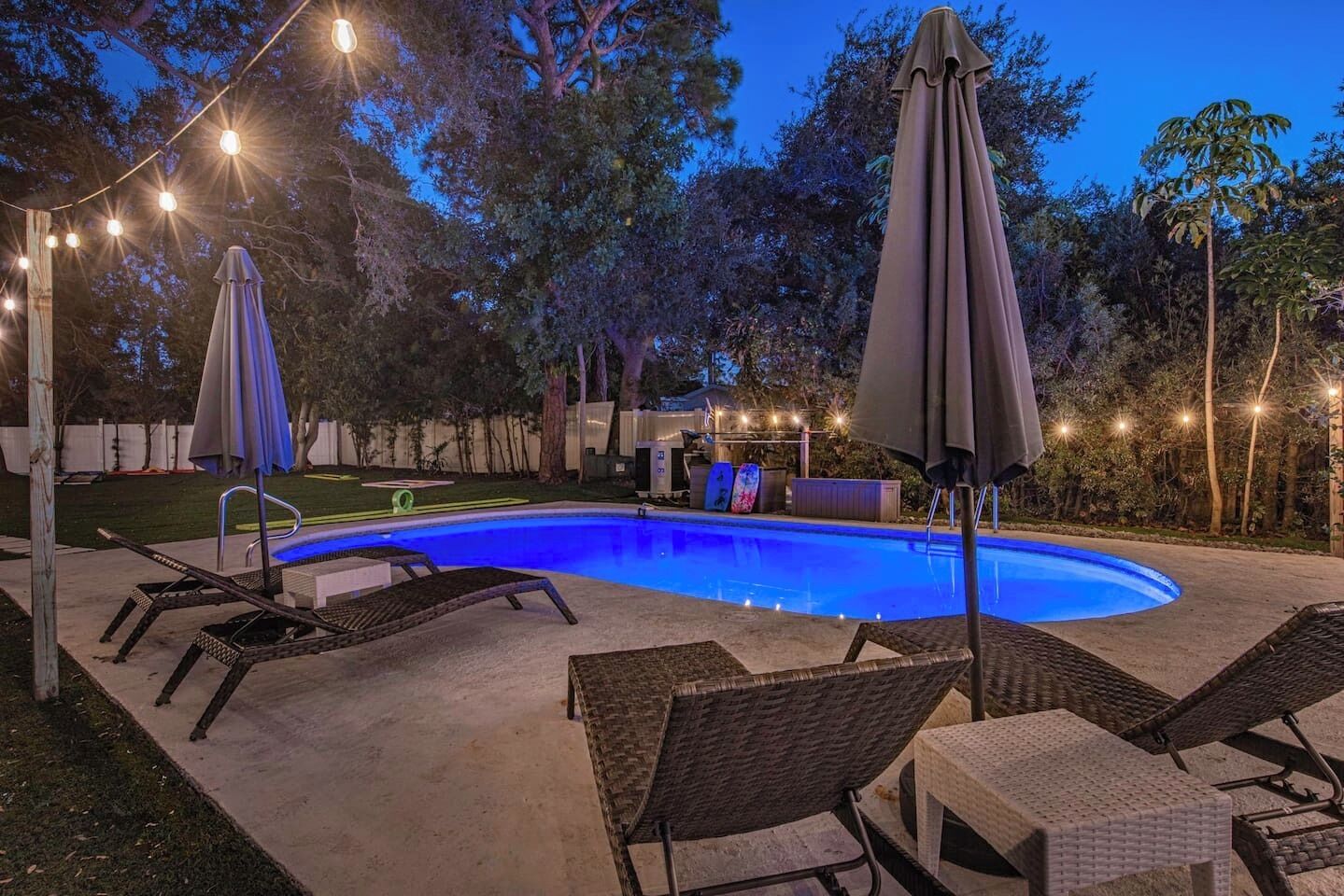 A swimming pool with lounge chairs and umbrellas, surrounded by trees and string lights.