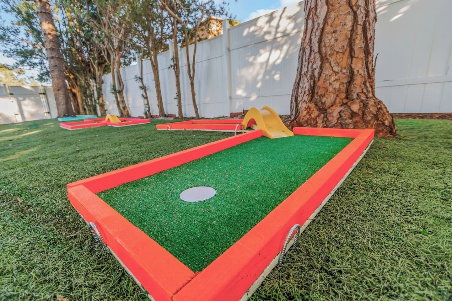 Un campo de mini golf con superficie verde, bordes rojos y un hoyo amarillo.