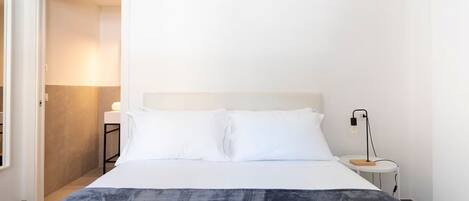 Une chambre d’hôtel avec un lit, une table de chevet avec une lampe et une porte donnant sur une autre pièce.