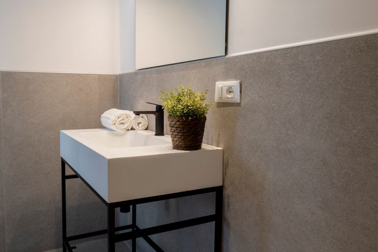 A modern bathroom with a white sink, a towel, and a potted plant.