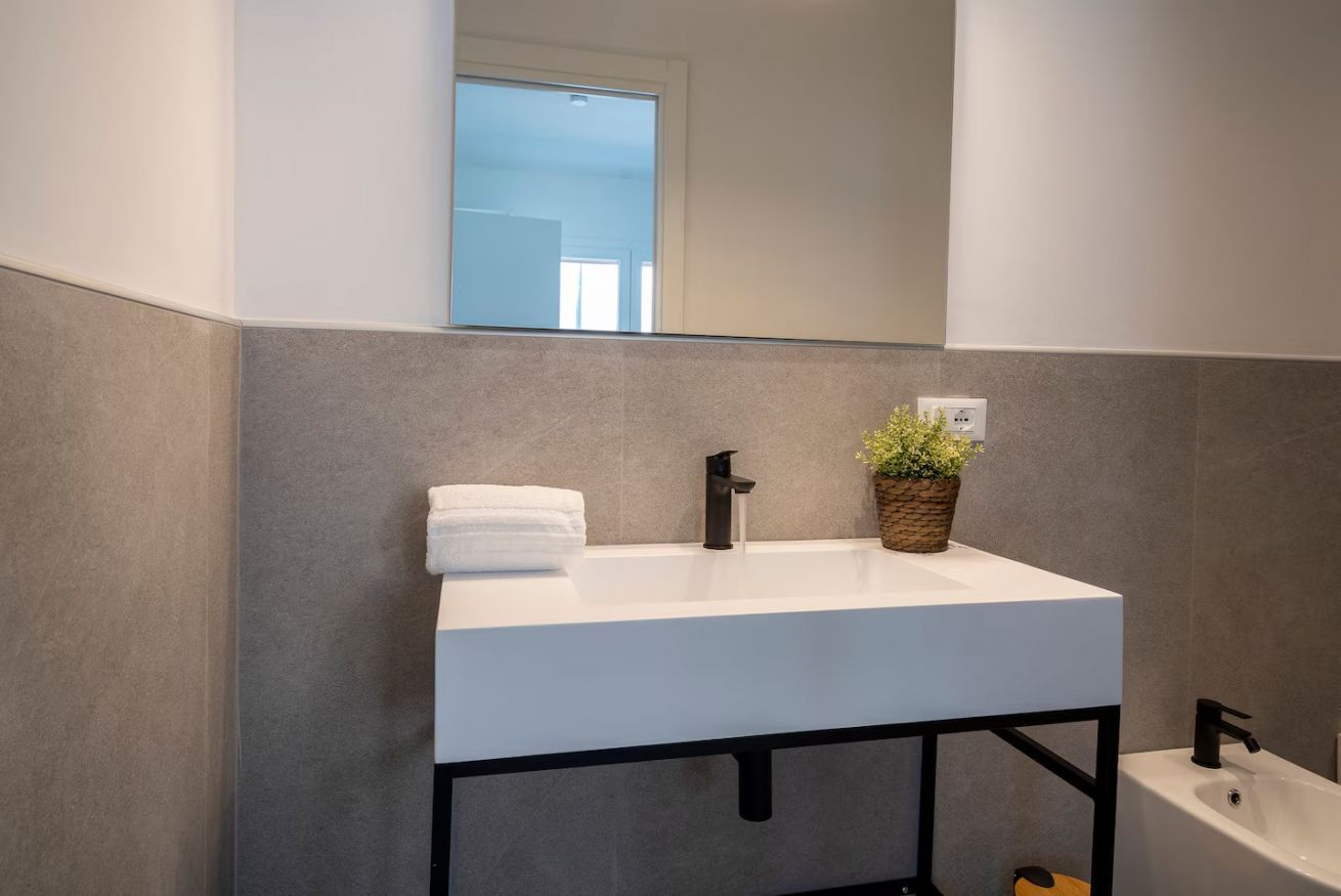 Un bagno moderno con lavandino bianco, rubinetto nero e una pianta in vaso.
