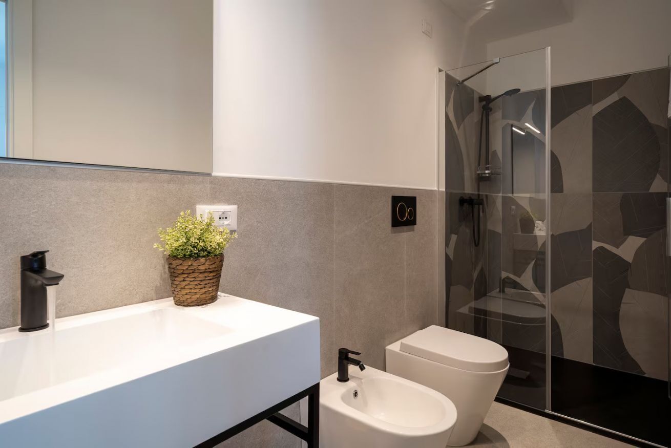 Un bany modern amb un rentapeus blanc, un vàter i una cabina de dutxa de vidre.