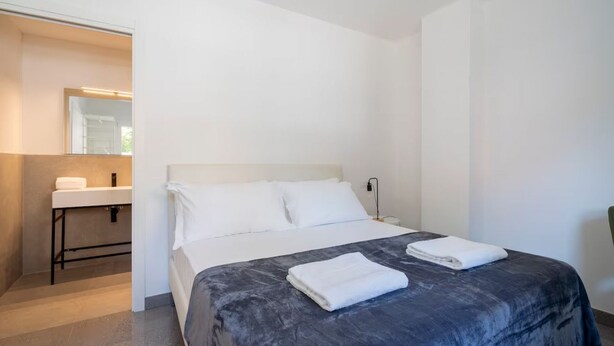 A hotel room with a bed, a bedside table, a nightstand, a mirror, and a bathroom with a sink and towel. - Marghera Smart Stay 1 | A Comfortable Room in Venice (Marghera)
