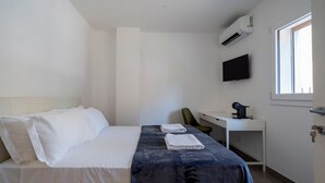 A hotel room with a bed, a desk, a chair, a TV, and an air conditioning unit. - Marghera Smart Stay 1 | A Comfortable Room in Venice (Marghera)