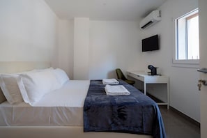 Una camera d'albergo con un letto, una scrivania, una sedia, una TV e un climatizzatore.