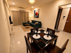 A modern living room with a sectional sofa, a dining table set for four, and a flat-screen TV mounted on the wall. - Premium 2-bedroom apartment in the hearts of Mumbai! (Mumbai)