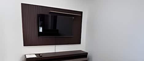 A modern bedroom with a large bed, a flat-screen TV mounted on the wall, and a minimalist design.
