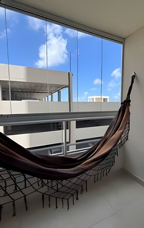 A hammock in a room with a large window, a balcony, and a view of buildings. - Apto 2 Qtos I Suíte I Lazer completo (Cabedelo)