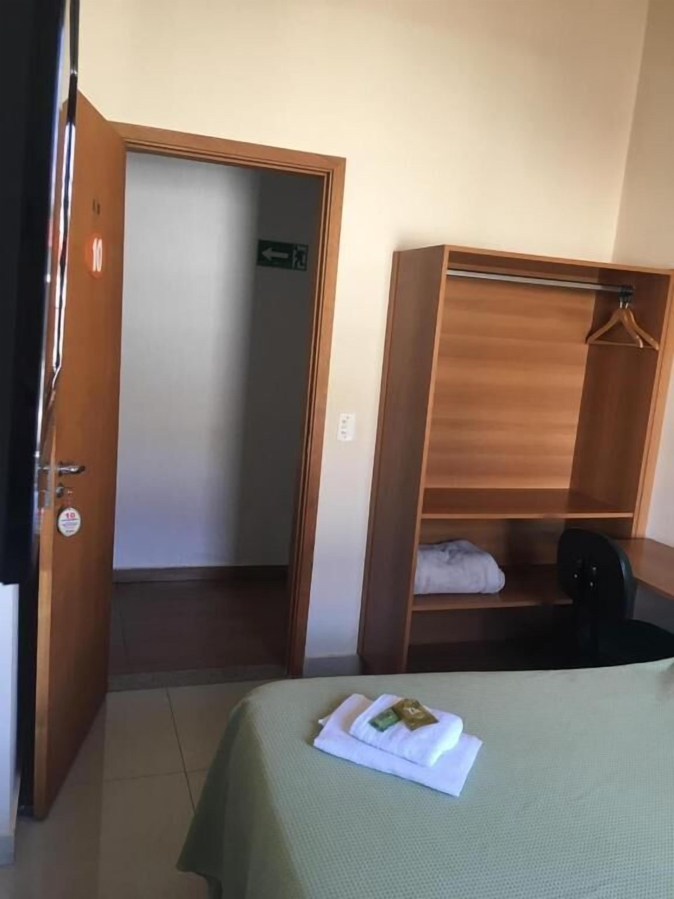 A hotel room with a bed, a wooden wardrobe, a door, and a small table.