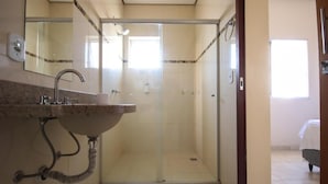 Ein Badezimmer mit einer Duschkabine aus Glas, einem Waschbecken mit Marmorplatte und einem Spiegel darüber.